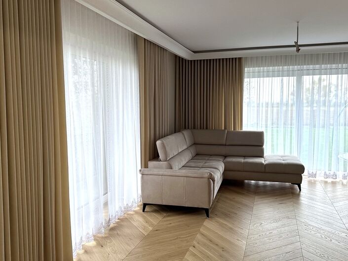 Ein modernes Wohnzimmer mit zarten Gardinen und beigen Vorhängen.